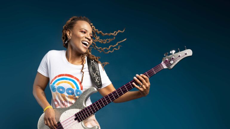 Photo of artist Divinity Roxx holding her bass guitar and smiling.