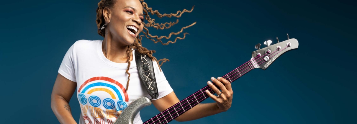 Photo of artist Divinity Roxx holding her bass guitar and smiling.