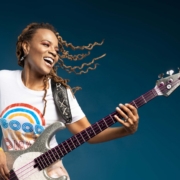 Photo of artist Divinity Roxx holding her bass guitar and smiling.