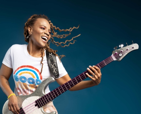 Photo of artist Divinity Roxx holding her bass guitar and smiling.